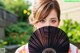 A woman holding a black fan in front of her face.